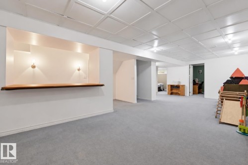 Expansive carpeted area with a built-in wood bar, wall sconces, and a paneled ceiling - 11423 35 Avenue Nw, Edmonton, AB 