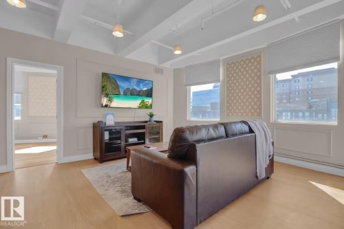 Wood-finish flooring, multiple windows with blinds, recessed decorative wall panels, and exposed beam ceilings with pendant lighting - #904 10105 109 St Nw, Edmonton, AB 