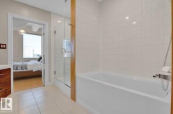 White tiled bathroom featuring a built-in bathtub, glass-enclosed shower, and wood-finish vanity with a light-colored countertop - 