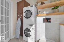 Stacked washer and dryer units, wood-finish cabinetry, white tile backsplash, wood shelving, and a French panel door - 