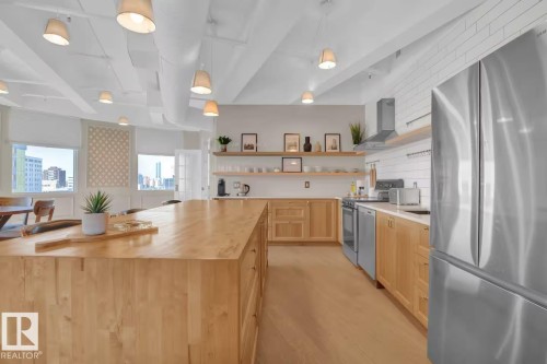 Spacious kitchen featuring a large wood island, light wood cabinetry, stainless steel appliances, white subway tile backsplash, and exposed ductwork - #904 10105 109 St Nw, Edmonton, AB 