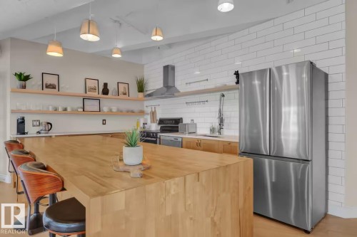 Expansive wood-finish island with seating, stainless steel French door refrigerator, white subway tile backsplash, stainless steel range hood, and open shelving - #904 10105 109 St Nw, Edmonton, AB 