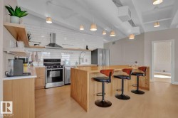 Kitchen featuring stainless steel appliances, a subway tile backsplash, light wood-finish cabinetry, an extended island with seating, and exposed ceiling ductwork - 