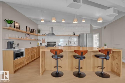 Kitchen with wood-finish flooring, light wood cabinetry, open shelving, stainless steel appliances, and a central island with an integrated breakfast bar - #904 10105 109 St Nw, Edmonton, AB 