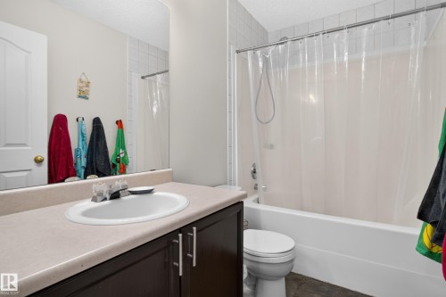 Full-width mirror, single vanity with a laminate countertop, dark wood-finish cabinetry, and a bathtub with a tiled shower surround - 9826 180 Avenue Nw, Edmonton, AB 