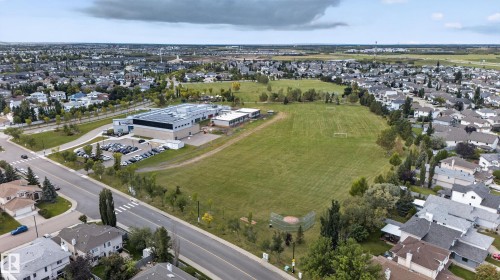 Expansive community featuring residential properties, a large educational facility, a dedicated parking area, and extensive green spaces with recreational fields - 9826 180 Avenue Nw, Edmonton, AB 