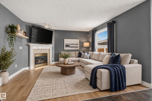 Corner-set fireplace with a mantle, wood-finish flooring, and a large window - 9826 180 Avenue Nw, Edmonton, AB 
