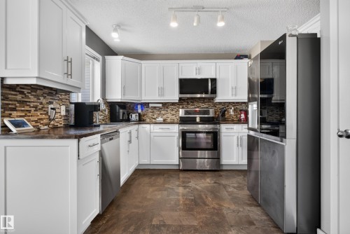 White cabinetry, stainless steel appliances, mosaic tile backsplash, dark wood-finish flooring, and recessed ceiling lighting - 9826 180 Avenue Nw, Edmonton, AB 