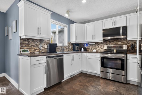White cabinetry with brushed nickel hardware, stainless steel appliances, dark countertops, and a mosaic tile backsplash - 9826 180 Avenue Nw, Edmonton, AB 