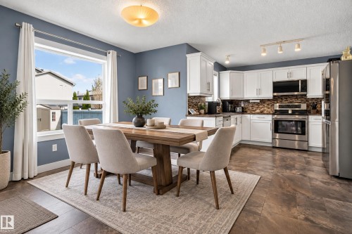 Open-concept living area with wood-finish flooring, a large window, white cabinetry, stainless steel appliances, and a tiled backsplash - 9826 180 Avenue Nw, Edmonton, AB 