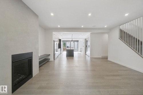 Light wood-finish flooring, recessed lighting, and a modern fireplace with a black surround - 10925 University Avenue Nw, Edmonton, AB 