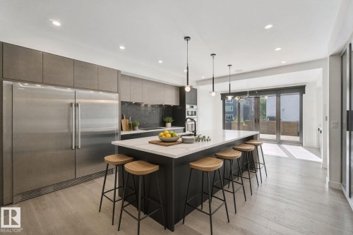 Gourmet kitchen with stainless steel appliances, a large island with seating, a dark tile backsplash, and light wood-finish flooring - 10925 University Avenue Nw, Edmonton, AB 