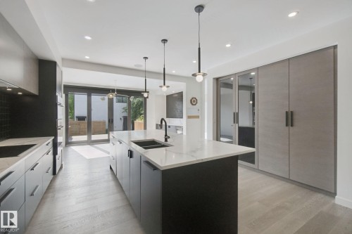 Kitchen featuring a large central island with an undermount sink, pendant lighting, built-in appliances, and light wood-finish flooring - 10925 University Avenue Nw, Edmonton, AB 