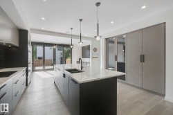 Kitchen featuring a large central island with an undermount sink, pendant lighting, built-in appliances, and light wood-finish flooring - 