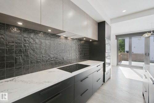 Kitchen featuring dark cabinetry, light countertops, a dark tile backsplash, and built-in wall ovens - 10925 University Avenue Nw, Edmonton, AB 