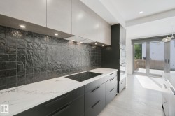 Kitchen featuring dark cabinetry, light countertops, a dark tile backsplash, and built-in wall ovens - 
