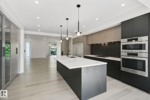 Modern kitchen featuring a large island with white countertop, integrated sink, and matte black faucet - 10925 University Avenue Nw, Edmonton, AB 