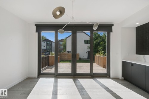 Full-light sliding glass doors, contemporary overhead lighting, wood-finish flooring, and built-in cabinetry with a light-toned countertop - 10925 University Avenue Nw, Edmonton, AB 