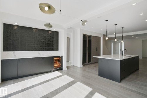 Open-concept living area with light wood-finish flooring, recessed lighting, and a kitchen island featuring a black faucet and three pendant lights - 10925 University Avenue Nw, Edmonton, AB 