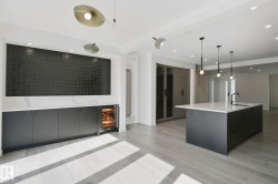 Open-concept living area with light wood-finish flooring, recessed lighting, and a kitchen island featuring a black faucet and three pendant lights - 
