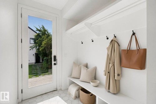 White mudroom with built-in bench, hexagon tile flooring, and integrated coat hooks - 10925 University Avenue Nw, Edmonton, AB 