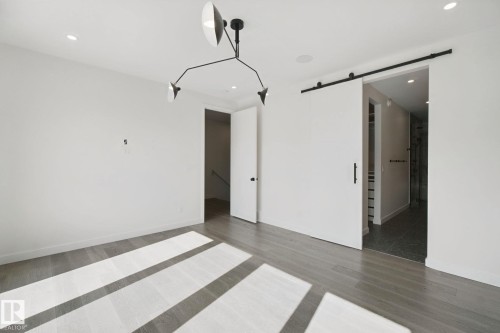 Recessed lighting, wood-finish flooring, modern chandelier, white walls, and a sliding barn door with black hardware - 10925 University Avenue Nw, Edmonton, AB 