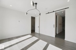 Recessed lighting, wood-finish flooring, modern chandelier, white walls, and a sliding barn door with black hardware - 