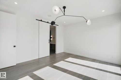Spacious room featuring wood-finish flooring, recessed lighting, a modern chandelier, and a barn door entry - 10925 University Avenue Nw, Edmonton, AB 