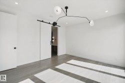 Spacious room featuring wood-finish flooring, recessed lighting, a modern chandelier, and a barn door entry - 