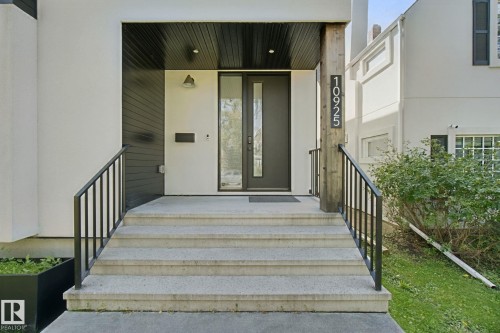 Concrete steps with metal railings leading to an entryway featuring a dark wood-finish ceiling, a modern front door with vertical glass insert, and an exterior wall sconce - 10925 University Avenue Nw, Edmonton, AB 