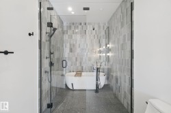 Glass-enclosed shower with matte black hardware, a freestanding bathtub, and floor-to-ceiling tile - 