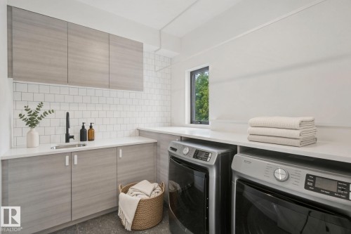 Laundry area featuring light wood-finish cabinetry, white subway tile backsplash, a sink with a black faucet, and a light-colored countertop - 10925 University Avenue Nw, Edmonton, AB 