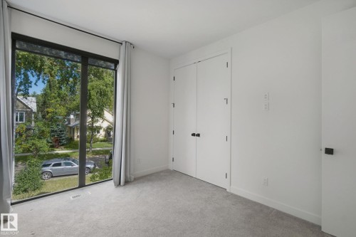 Floor-to-ceiling window with black trim, light gray carpeting, double closet doors with black hardware, white walls, and a white door with black hardware - 10925 University Avenue Nw, Edmonton, AB 