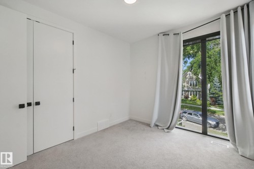 White walls, light carpet flooring, large window, full-height curtains, and double closet doors with dark hardware - 10925 University Avenue Nw, Edmonton, AB 