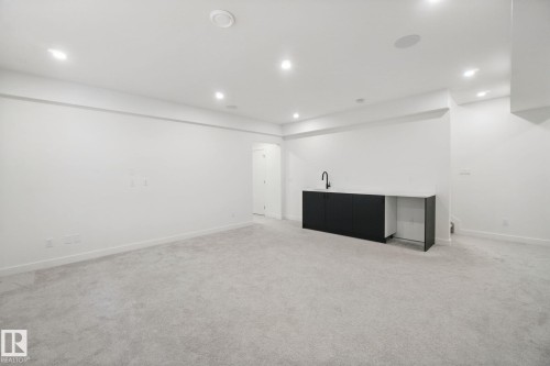Recessed lighting illuminates the carpeted floor and built-in wet bar featuring dark cabinetry, a white countertop, and a matte black faucet - 10925 University Avenue Nw, Edmonton, AB 