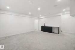 Recessed lighting illuminates the carpeted floor and built-in wet bar featuring dark cabinetry, a white countertop, and a matte black faucet - 