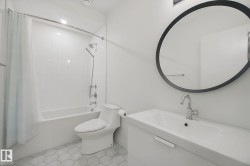 White bathroom featuring a built-in tub with tile surround, hexagonal floor tiles, a vanity with an integrated sink, a chrome faucet, and a round wall mirror - 