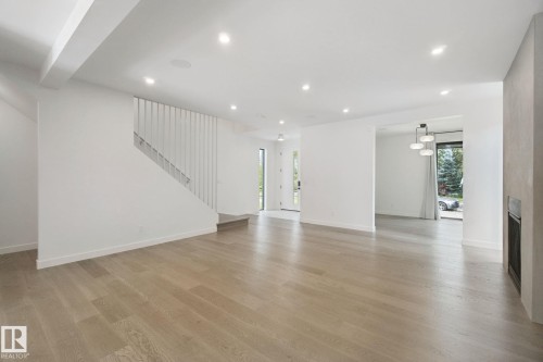 Open concept living space featuring wide plank wood-finish flooring, recessed lighting, a modern staircase, and a built-in fireplace - 10925 University Avenue Nw, Edmonton, AB 
