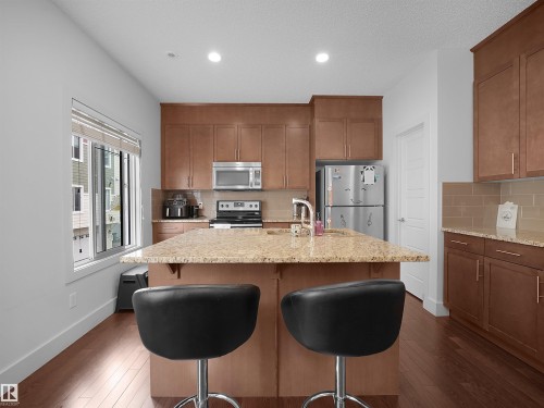 Kitchen featuring a central island with countertop seating, wood-finish flooring, stainless steel appliances, and wood cabinetry - #40 2003 Rabbit Hill Rd Nw, Edmonton, AB 