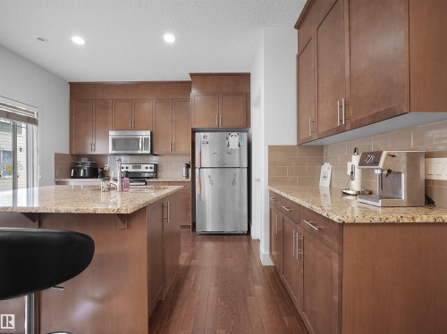Kitchen featuring wood-finish cabinetry, granite countertops, stainless steel appliances, and a tiled backsplash - #40 2003 Rabbit Hill Rd Nw, Edmonton, AB 