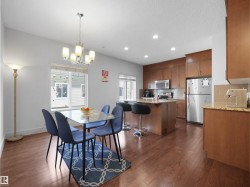 Open-concept kitchen and dining area featuring wood-finish flooring, wood cabinetry, stainless steel appliances, and stone countertops - 