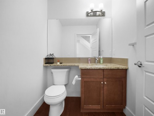 Powder room featuring a vanity with a light-colored stone countertop, wood-finish cabinetry, a built-in sink, and a large wall-mounted mirror - #40 2003 Rabbit Hill Rd Nw, Edmonton, AB 