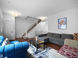 Wood-finish flooring throughout, white paneled door, staircase with carpeted treads and metal balusters, and ceiling-mounted light fixtures - 