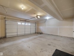 Spacious garage featuring a sectional overhead door with transom windows, exposed ceiling beams, and concrete flooring - 