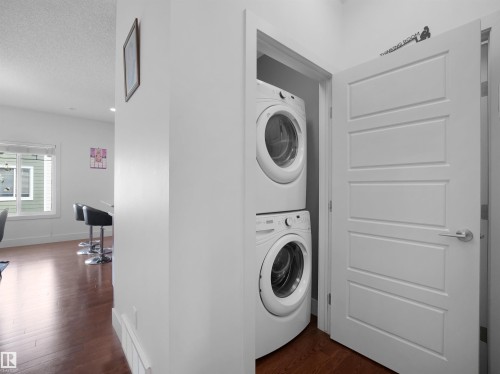 Stackable washer and dryer appliances, wood-finish flooring, white trim, and a contemporary panel door - #40 2003 Rabbit Hill Rd Nw, Edmonton, AB 
