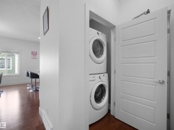 Stackable washer and dryer appliances, wood-finish flooring, white trim, and a contemporary panel door - 