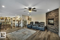 Living room featuring a stacked stone fireplace with a black insert, wood-finish flooring, and recessed lighting - 