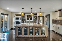 Spacious kitchen featuring a large central island with glass-front cabinetry, granite countertops, built-in stainless steel appliances, and dark tile flooring - 
