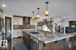 Spacious kitchen featuring a large island with an undermount sink, pendant lighting, stainless steel appliances, and a mosaic tile backsplash - 