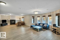 Spacious living area featuring light wood-finish flooring, a contemporary fireplace with a dark surround, and a curved wall with multiple windows - 